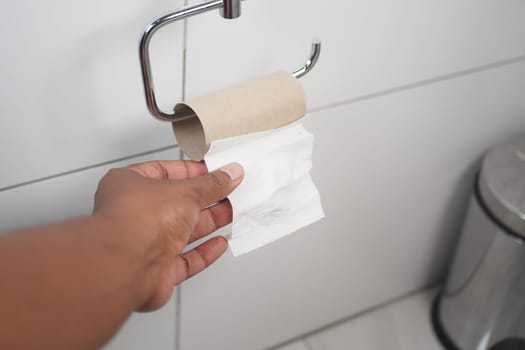 A hand pulls toilet paper from a roll in a clean bathroom.