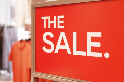 Bright red sign announces a sale at a retail location with clothing items.