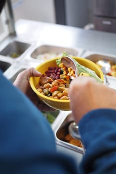 A person holds a yellow bowl filled with fresh vegetables and beans.
