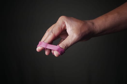 Close-Up of Hand with Pink Finger Exercise Tool Against Dark Background.