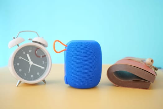 A blue portable speaker is placed between a clock and a shoe.