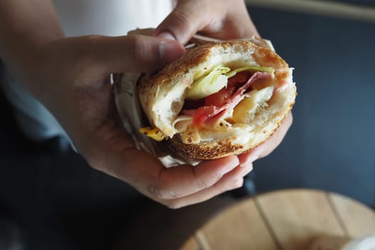 A person holds a fresh sandwich filled with ingredients at a cafe.