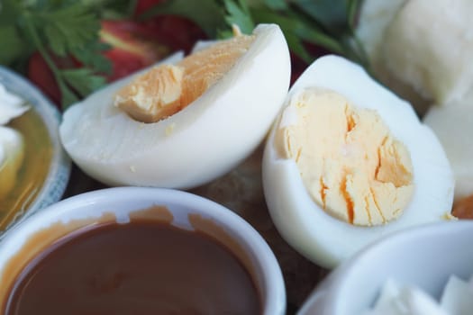 Boiled eggs cut in half alongside a savory dipping sauce and fresh herbs.