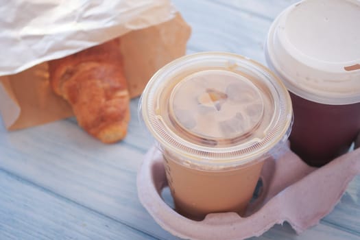 Iced coffee and a warm croissant are placed on a blue wooden table.