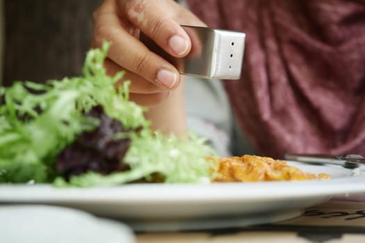A hand sprinkles salt onto a dish containing salad and pasta.