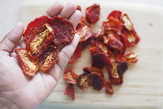 A hand holds dried tomatoes with more pieces scattered on a board.