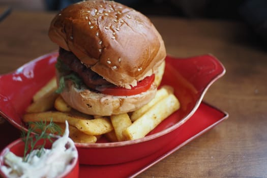 A mouthwatering hamburger topped with vegetables on a red dish with fries.