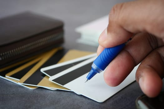 A person is using a blue pen to write on a blank card next to a wallet.