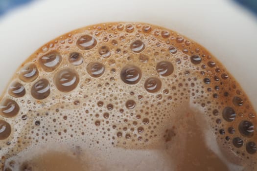 Foam rises above a coffee in a white cup, inviting enjoyment.