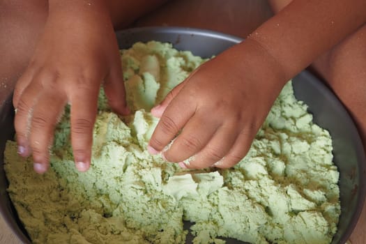 A child explores textured green sand with their hands in a tray.