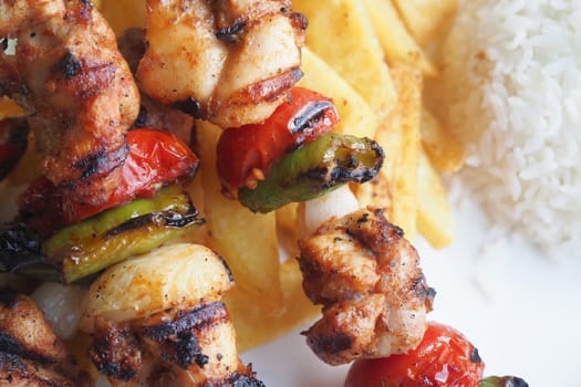 Juicy grilled chicken skewers with vegetables alongside rice and fries.