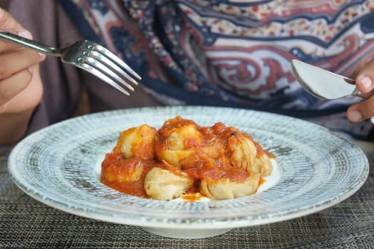 A person savors delicious dumplings topped with tomato sauce.