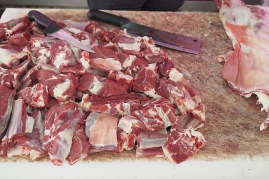 Butcher is cutting various meat pieces on a wooden block.