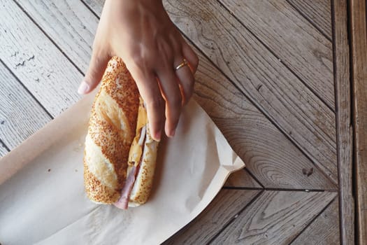 A hand is about to grab a sandwich placed on parchment paper.