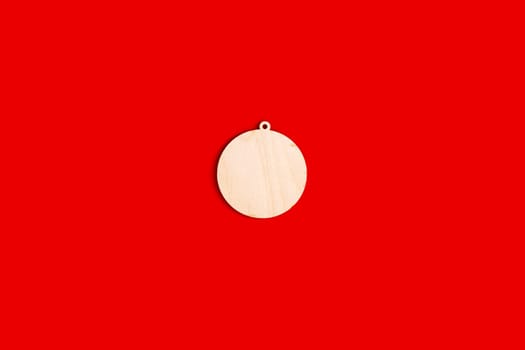 Wooden, flat, natural, unpainted shape of a Christmas ball on a red background. Close up. Copy space. Mock up. Top view