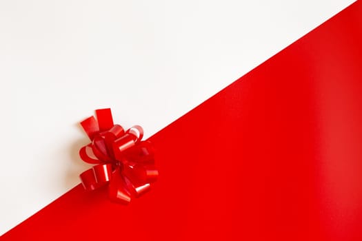 Red plastic bow on a red and white diagonal paper texture, lies in the middle, background for a template, horizontal. View from above. Mock up