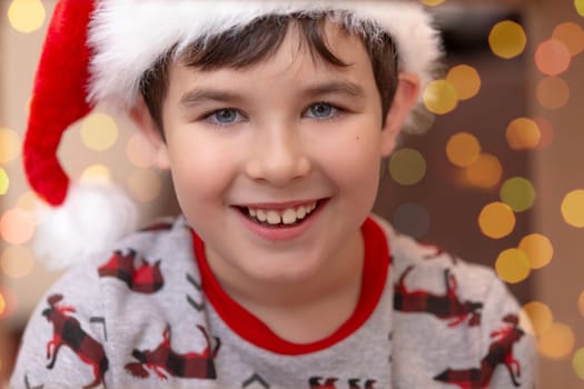 Close up portrait of a handsome smiling European boy in a red cap on the background of bokeh of New Year's garlands. Christmas and New Years concept.