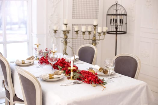 Festive Christmas and New Year table setting in natural and white colors with a red New Year garland and gold accessories, candles