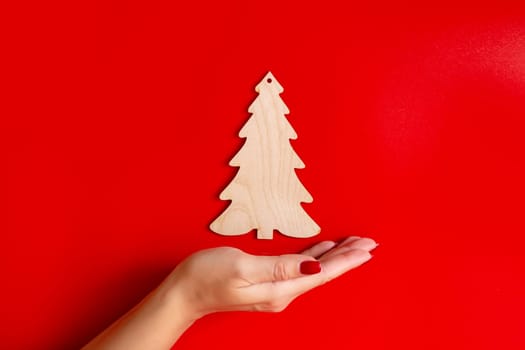 Flat natural unpainted wooden spruce shape on a female palm on a red background. Close up. Copy space . Mock up