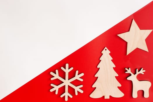 Flat natural unpainted wooden christmas decorations on red and white diagonal background: star, snowflake, deer and spruce. Copy space. Mock up