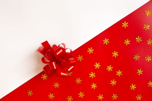 Red plastic bow on a red and white diagonal paper texture with golden snowflakes, lies in the middle, background for a template, horizontal. View from above. Mock up