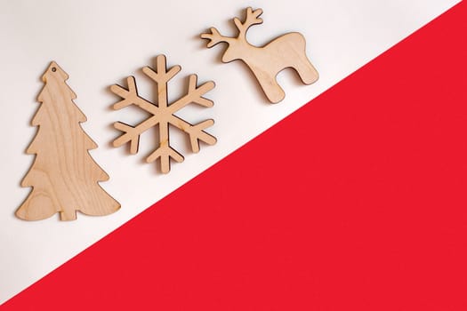 Flat natural unpainted wooden christmas decorations on white and red diagonal background: spruce, snowflake, deer. Copy space. Mock up