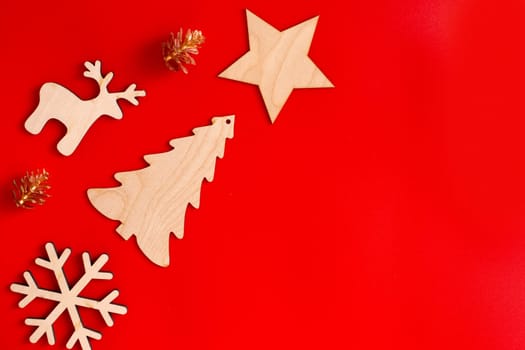 Flat natural unpainted wooden Christmas decorations: star, snowflake, deer and spruce and golden cones lie diagonally on red background. Copy space. Mock up