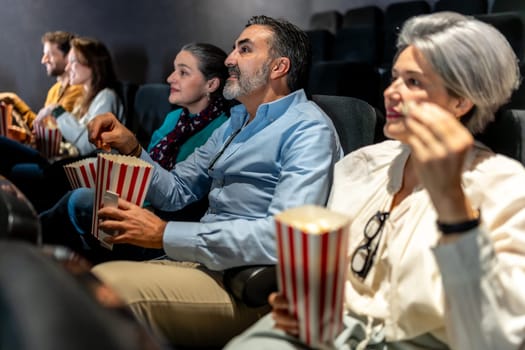 Group of friends sharing laughter and enjoying popcorn while watching an exciting film screening in a cozy movie theater