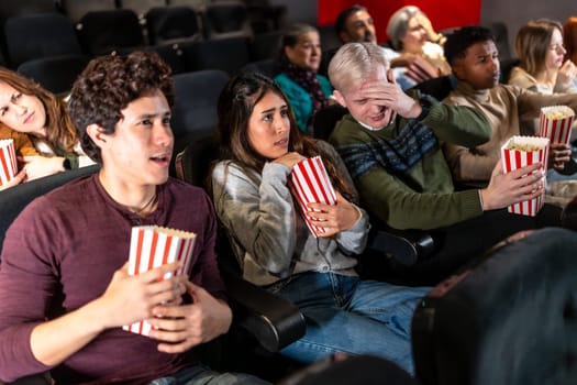 Young people and adults experiencing fear and suspense while watching a horror movie at the cinema, eating popcorn