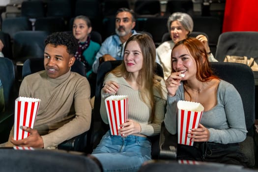 Group of friends watching a film at the movie theatre, eating popcorn and enjoying their leisure time