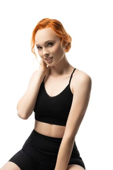 Self assured young fit female model with ginger hair in black sportswear smiling look at camera isolated
