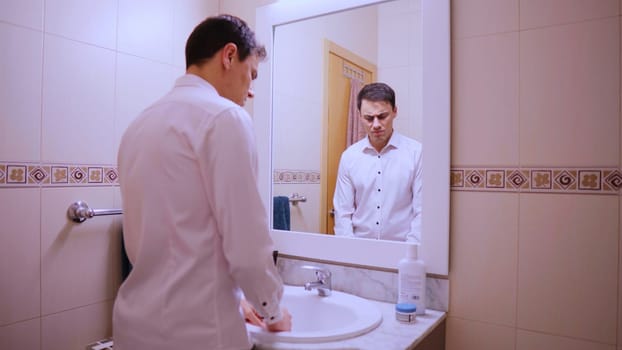 Sad and worried businessman looking at his reflection in the bathroom mirror