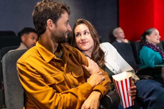 Couple enjoying a cozy movie night, sharing popcorn and affection while surrounded by a lively audience in a bustling cinema