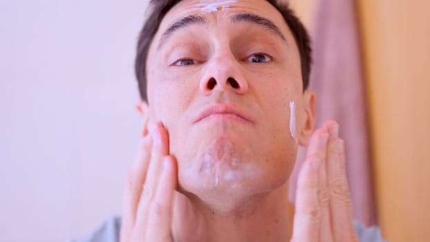 Caucasian man applying moisturizing cream on his face in the bathroom
