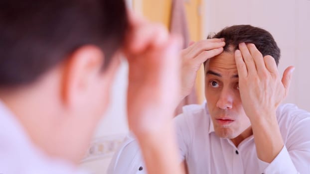 Worried businessman checking his receding hairline in the bathroom mirror