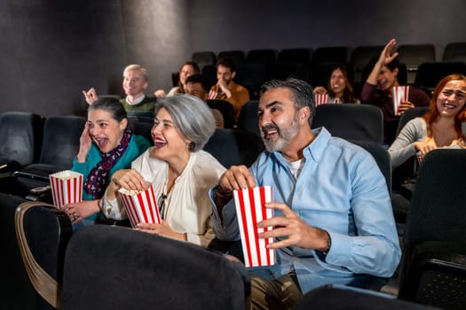 People of different ages laughing and eating popcorn while watching a movie at the cinema