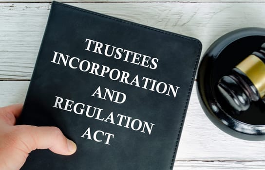 Hand holding Trustee Incorporation and Regulation Act book with gavel background.