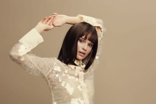 Woman, white shirt, beige background a woman in a white shirt poses with her hands on her head, her hair pulled back, in front of a beige background, exuding a sense of calm and confidence