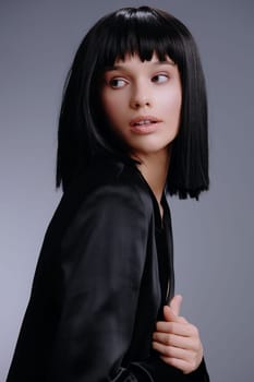 Woman with black hair and black jacket, standing with hands on hips, looking to the side, posing confidently against a plain background, capturing a stylish and thoughtful moment