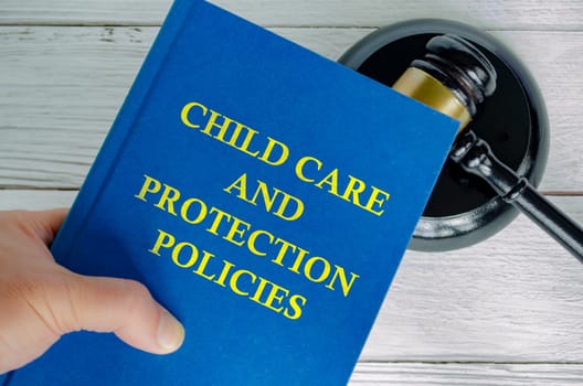 Hand holding Child Care and Protection Policies book with gavel background.