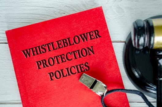 Top view of Whistleblower Protection Policies book with whistle and gavel background.