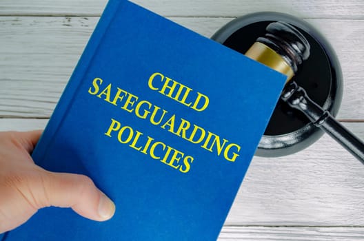 Hand holding Child Safeguarding Policies book with gavel background.