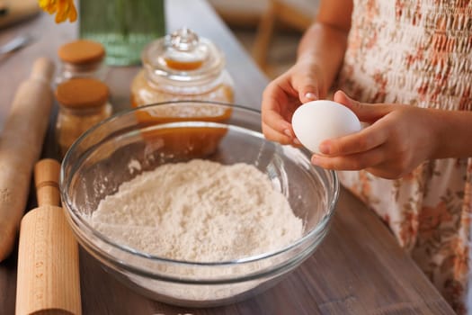 Child holding egg over bowl of flour preparing to bake, cozy kitchen scene with baking tools and ingredients.