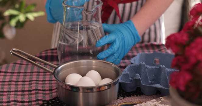 Hands in blue gloves fill a pot with water for boiling eggs, getting ready for decorating Easter eggs. This activity fosters creativity and festive spirit.