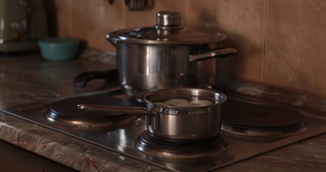On the stove, a small pot holds boiled eggs while another larger pot simmers nearby. This setting highlights the process of cooking, emphasizing the use of organic egg ingredients for a healthy dish.