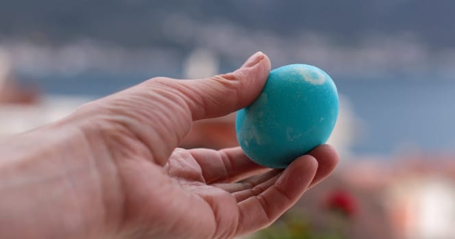 A person holds a beautifully colored turquoise Easter egg against a scenic backdrop, perfect for celebrating the joys of coloring and decorating during Easter festivities.
