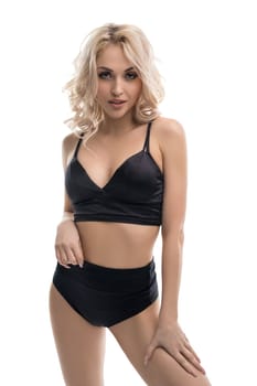 Alluring blond female wearing black underwear standing against white background in studio and looking at camera