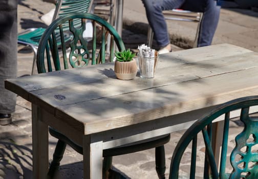 Windsor, UK - Apr 03, 2025 - Sunlight shine through Wooden table and Green metal chairs outside a cafe on street in the afternoon. use it as your Wallpaper, Poster and Space for text, Selective focus.
