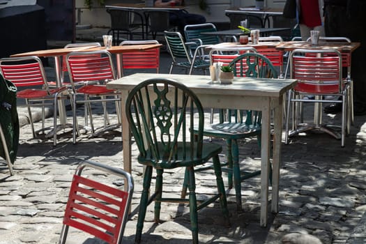 Windsor, UK - Apr 03, 2025 - Sunlight shine through Wooden table and Green metal chairs outside a cafe on street in the afternoon. use it as your Wallpaper, Poster and Space for text, Selective focus.