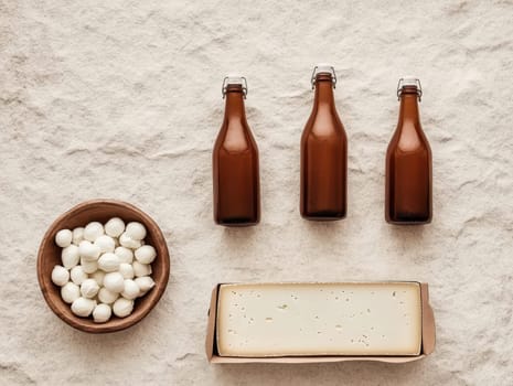 Three brown glass bottles, bowl of mozzarella balls, and a block of cheese sit on a light beige surface.